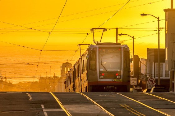 An N-Judah streetcar heads east on Judah Street in San Francisco as the sun sets in the background over the Pacific Ocean.