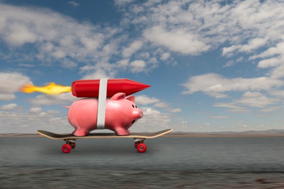 A piggy bank streaks down the road to riches on a skateboard and with a rocket strapped to his back.