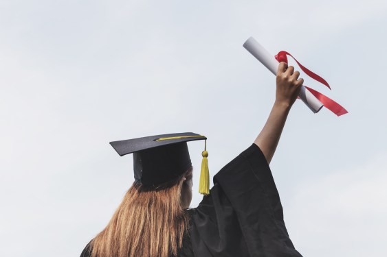 Rear view of woman in a cap and gown holding a diploma in the air.