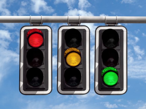 Image of red, yellow, and green traffic lights against a blue sky.