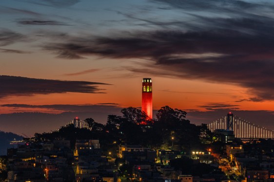 An aerial view of Coit Tower and the San Francisco Bay in the distance with a dramatic and vibrant sky.