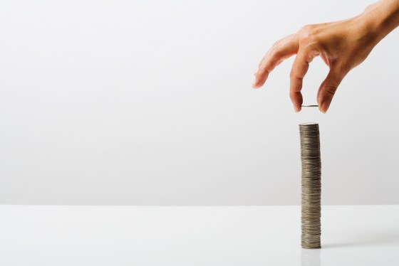 Image of a person's hand placing a coin atop a tall stack of coins.