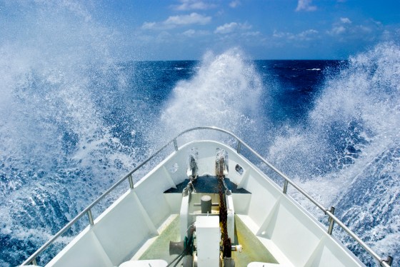 The bow of a ship ploughs through heavy seas and spray in open ocean.