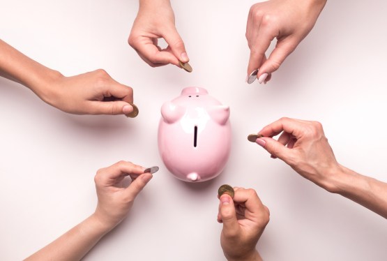 Hands holding coins around piggy bank