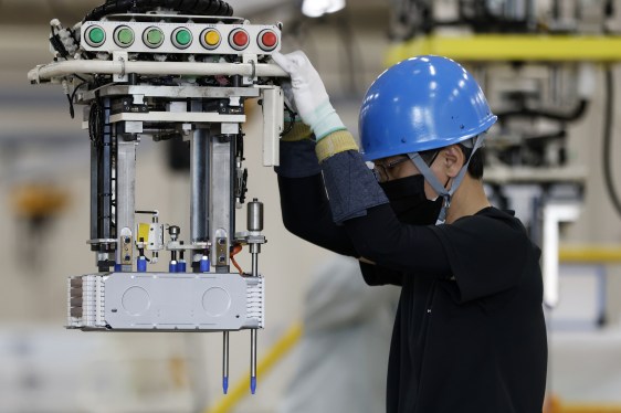 A worker wearing a blue hard hat moves a stack of batteries installing onto a battery pack for a kei electric vehicle (EV) on the production line