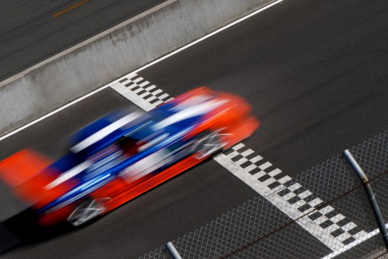 Blurred race car with nose of the finish line on a track.