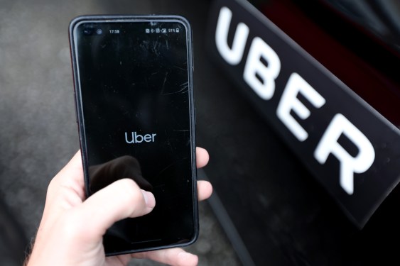 hand holding phone displaying Uber app next to Uber car