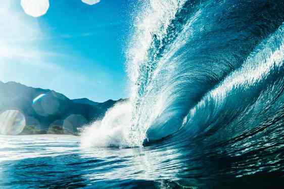 A wave crests off a mountainous shoreline.