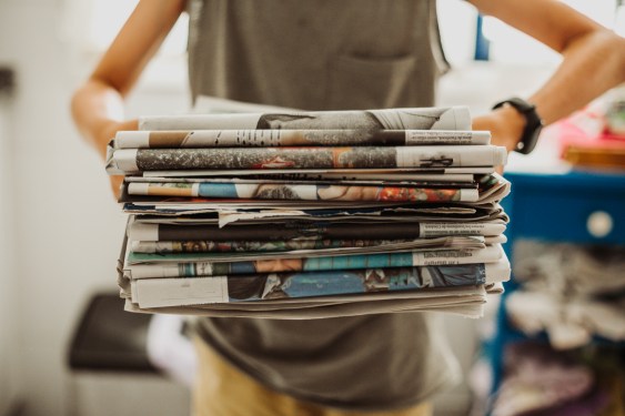 A person holding a pile of newspapers.