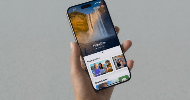 Apple Photos app gets a revamp for iOS 18. Hand holding an iPhone displaying Photos app