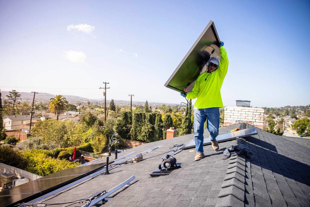 Man carrying a solar panel on a roof in Southern California.