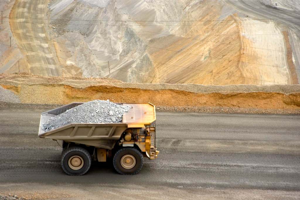 A large yellow dump truck carries ore out of a pit mine.
