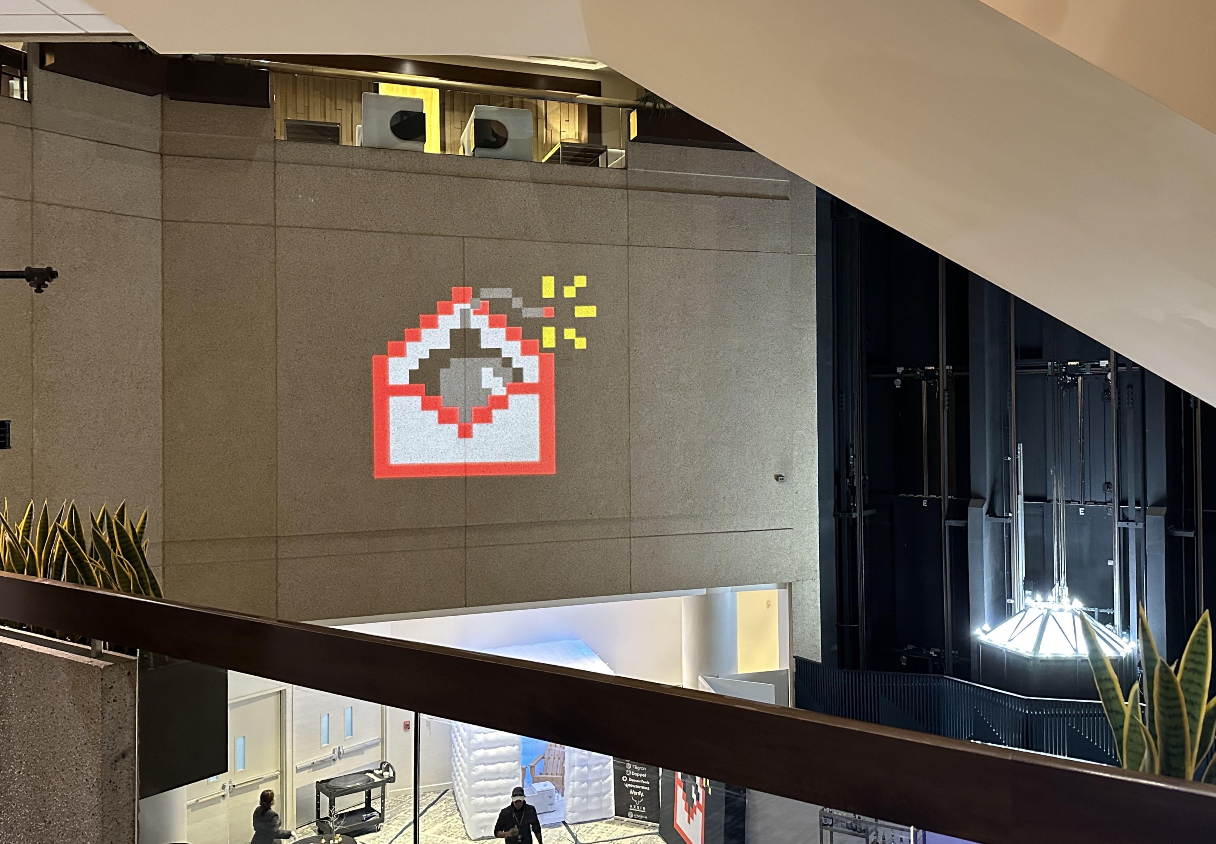 a photo from the top balcony of the Cyberwarconference in Washington DC on November 22. The photo shows the Cyberwarcon logo — a pixel-based cartoon bomb in a red cartoon envelope — projected on a wall of the conference.