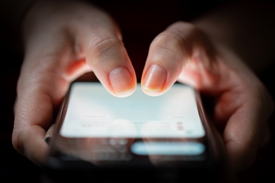 Close-up of two thumbs touching on a smartphone screen in the dark.