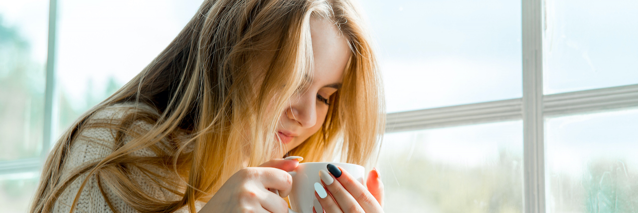 Woman holding a coffee mug sitting next to a window