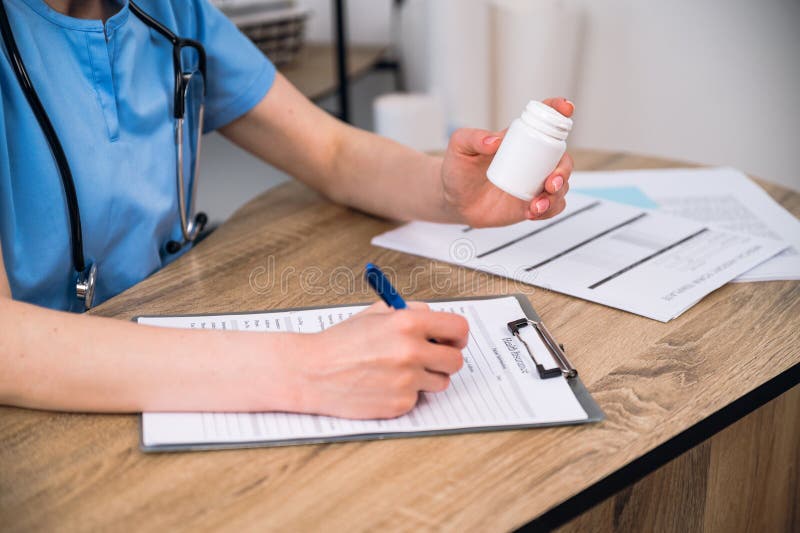 cropped shot of woman doctor hold pill medication in hand and filling medical insurance at desk in clinic cabinet. physician prescribe sedative tablet and make treatment plan for patient