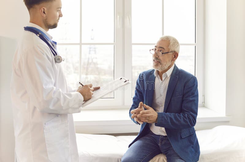 Elderly male patient having a conversation with a doctor during a consultation in a hospital office. The doctor or nurse provide care to the senior patient, ensuring health needs are met. Elderly male patient having a conversation with a doctor during a consultation in a hospital office. The doctor or nurse provide care to the senior patient, ensuring health needs are met.