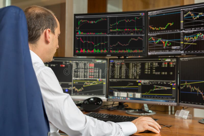 Rear view of stock trader analyzing data at multiple computer screens. stock photos