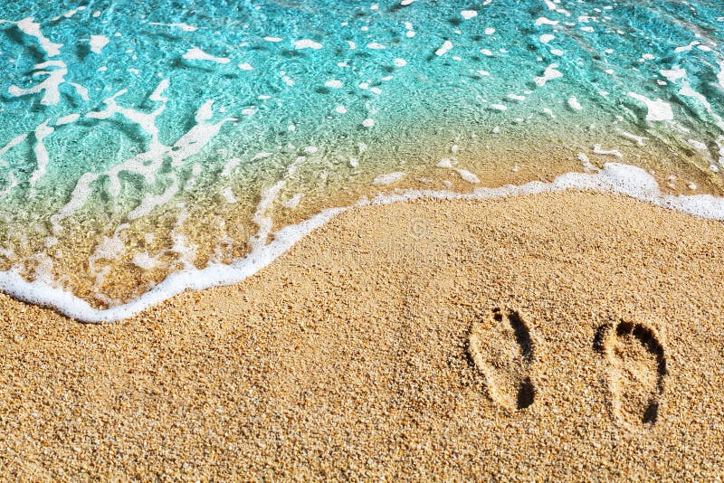 Two footprints on yellow sand, blue sea wave, white foam top view close up, turquoise ocean water, summer vacations concept stock images