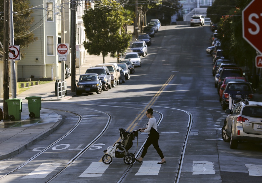 A woman walks with a child stroller across a pedestrian crossing, in San Francisco