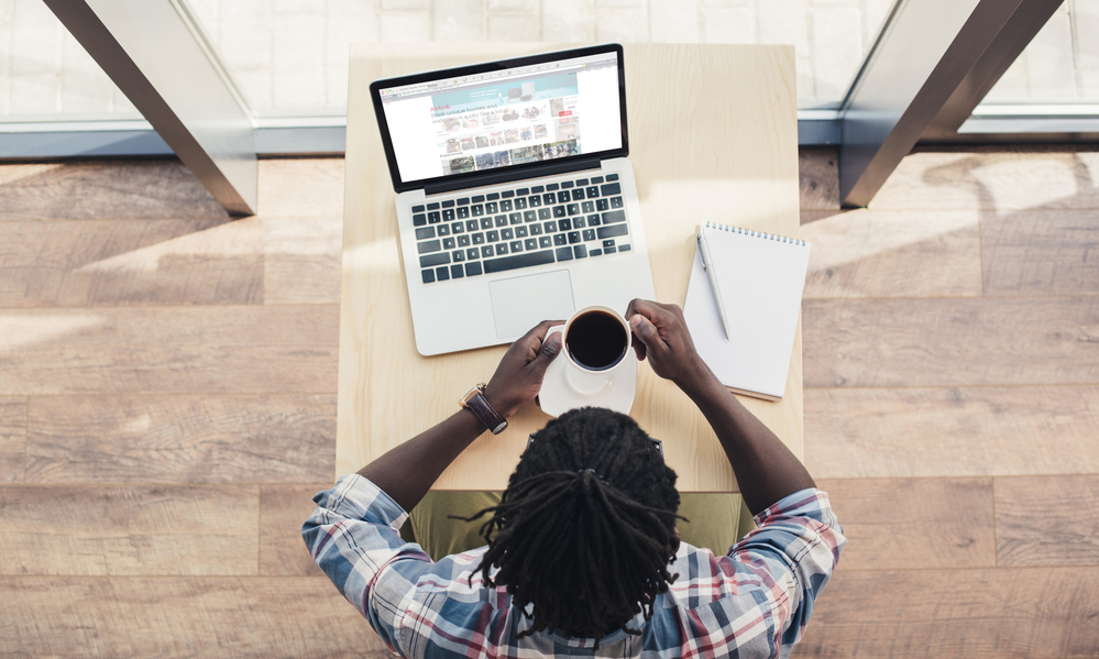 Overhead view of african american man drinking coffee and using laptop with airbnb website — Photo by IgorVetushko