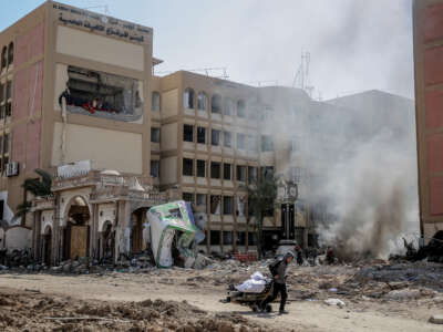 A young Palestinian pulls a wheel cart past the heavily damaged building of Al Azhar University in Gaza City on February 15, 2024.