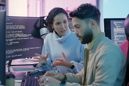 Computer programmer explaining code on a computer to a trainee programmer.