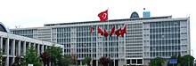 A mid-rise glass-paned office building, with an array of Turkish flags in the front.