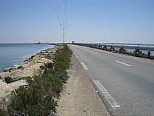 Perspective sur une route aménagée sur une digue entourée de part et d'autre par la mer ; un pipeline a été aménagé du côté droit.