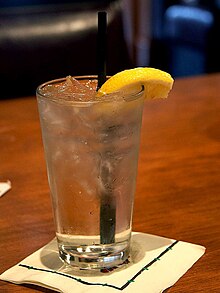 A clear glass filled with water, ice cubes, a slice of lemon, and a straw