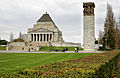 Uma visão da norte do Shrine mostrando muitos visitantes prestando respeito. A parada anual do ANZAC Day aproxima-se do Shrine do norte. Isto mostra as esculturas do lugar, claramente inspiradas pelo Parthenon. A figura central é a "chamada das armas"