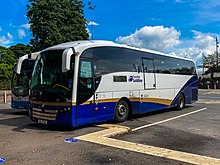 A white, blue and gold coach parked in a bus station.