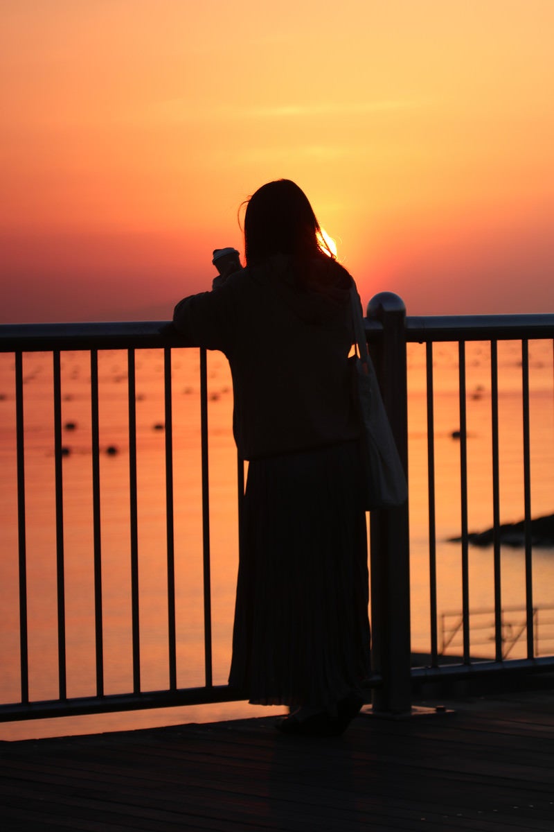 海を眺める女性と焼けた空の写真