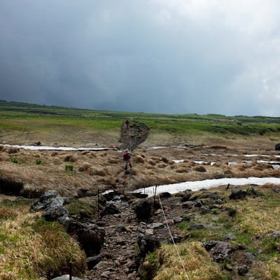 曇りの旭岳の登山道を歩く登山者の写真