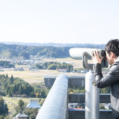 双眼鏡を覗き込む男性観光客の写真