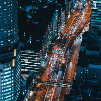 ビル群の間を通る幹線道路と車列（夜間）の写真