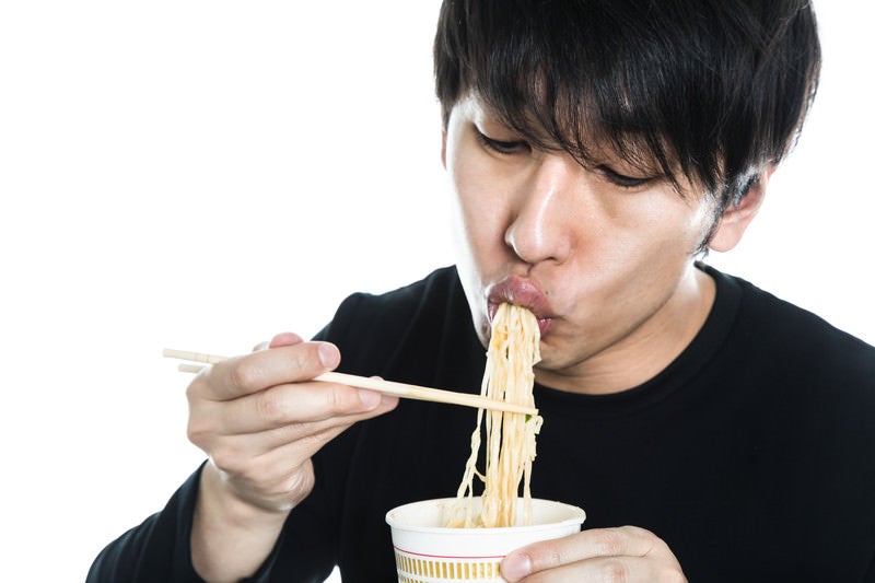 カップラーメンをすする男性の写真