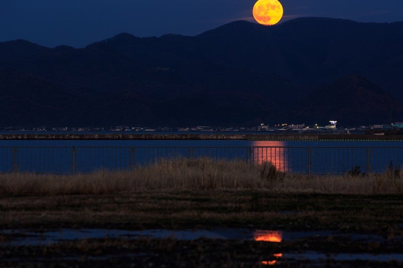 山の上から顔を出すスーパームーンの写真