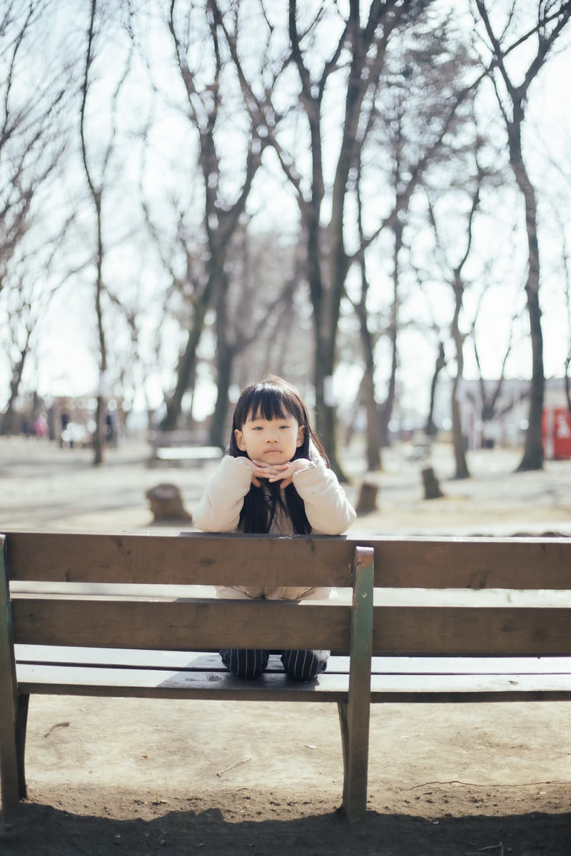 公園のベンチで退屈そうにする少女の写真