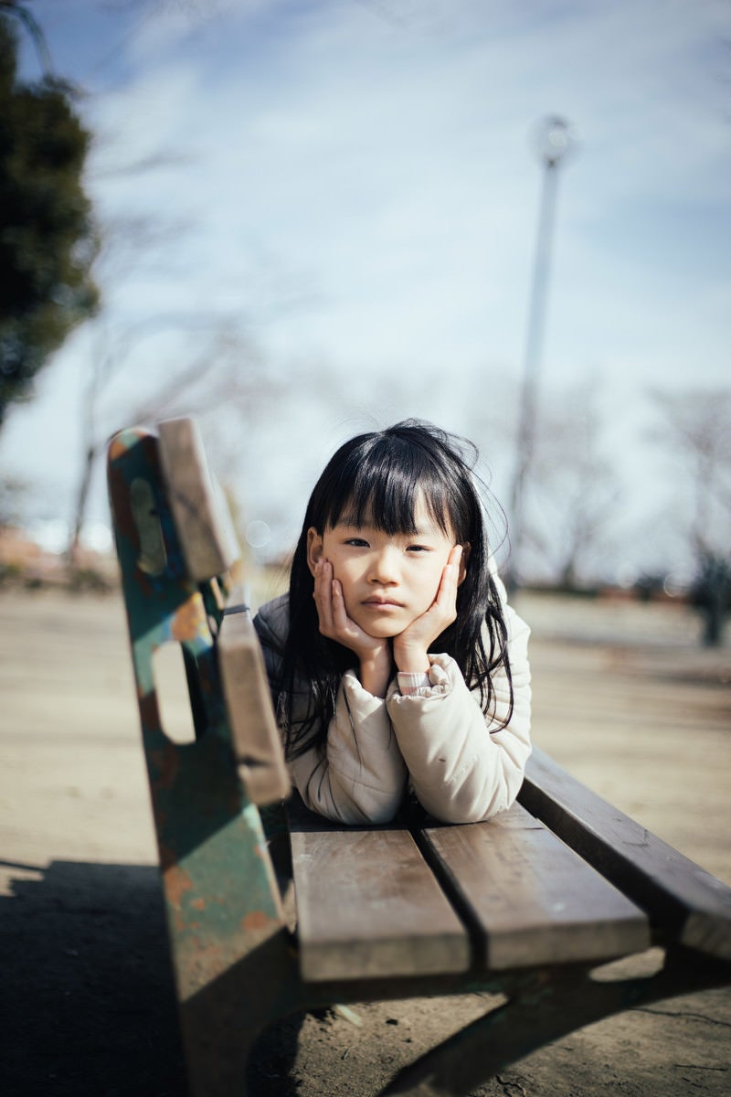 「親同士の会話が盛り上がりすぎてベンチで暇そうにする女の子」の写真［モデル：あんじゅ］