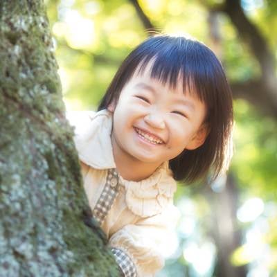 木陰からニコニコ笑顔の小さい女の子の写真