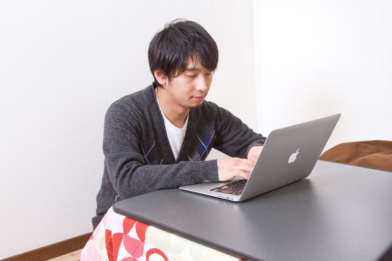 寒い日はこたつの上でPCを触る男性の写真