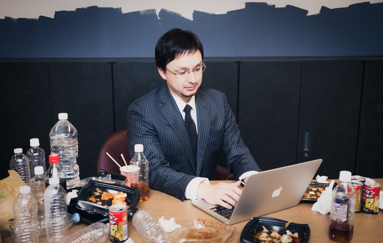 「飲みかけの大量のペットボトルと食べかけのカップラーメンを放置して仕事する同僚」の写真［モデル：Max_Ezaki］