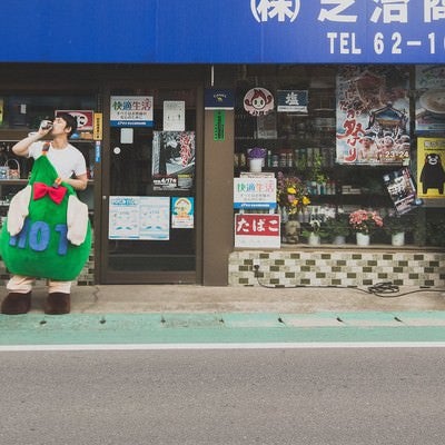 商店の前でコーヒーを飲むゆるキャラと中の人の写真