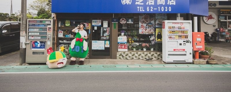 商店の前でコーヒーを飲むゆるキャラと中の人の写真