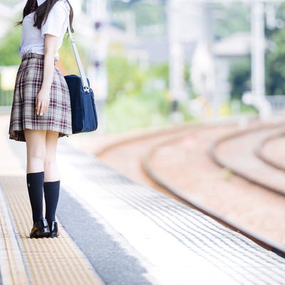 誰もいない駅のホームと振り返る女子高生の写真