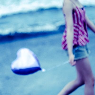 ハートを持って砂浜を歩く女性の写真