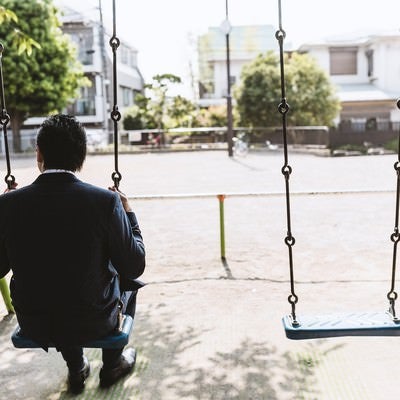 公園のブランコで時間を潰す後ろ姿が切ないビジネスマン（ドイツ人ハーフ）の写真