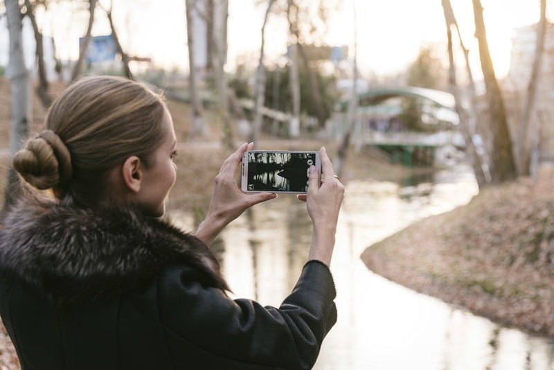 スマートフォンで景色を撮影するブロンド美女の写真