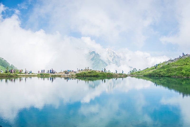 沸き立つ雲のリフレクションと登山者の列の写真